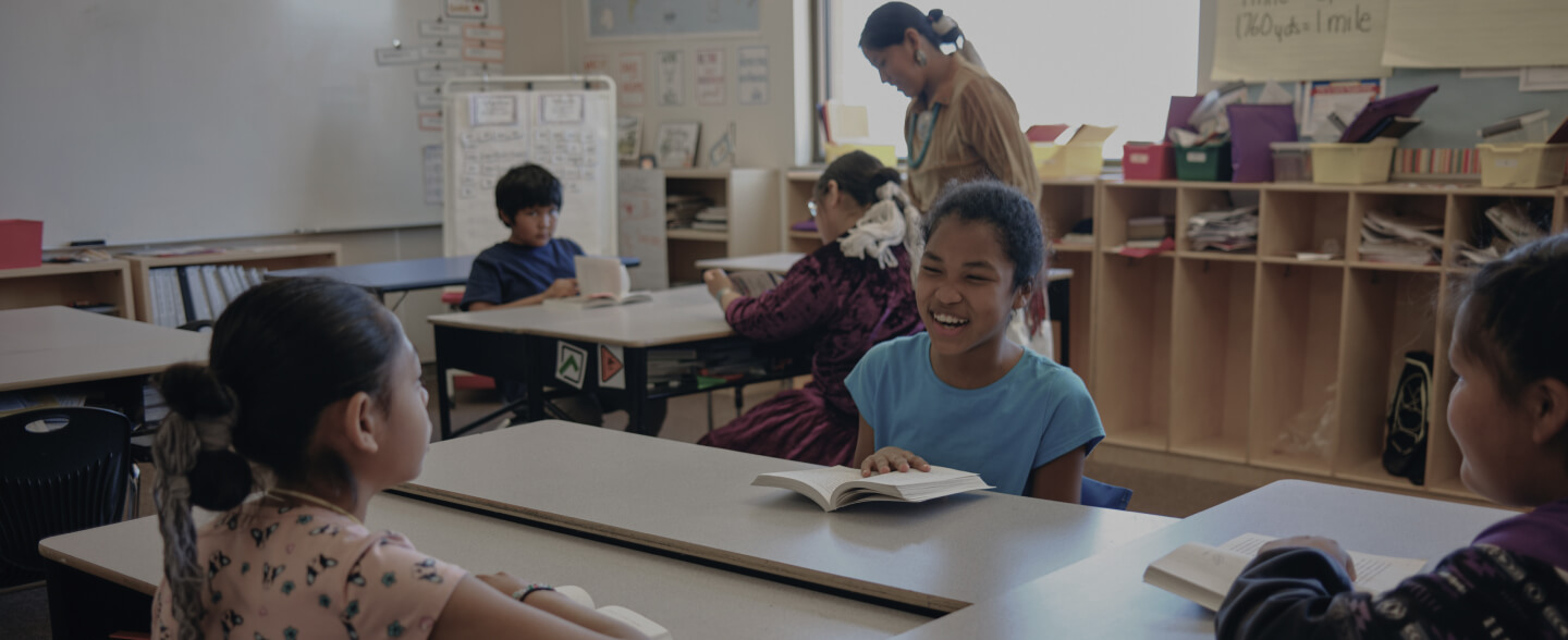 Kids in a classroom talking at their desks