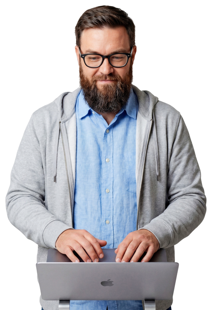 A professional man with glasses and a beard typing on a laptop, wearing a gray hoodie over a blue shirt